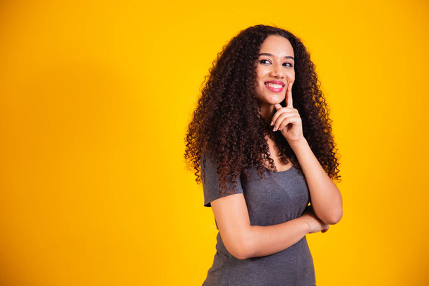 Portrait of beautiful young African American woman with curly hair thinking and having an idea on yellow background with space for text. good idea woman concept - Fotoğraf, Görsel