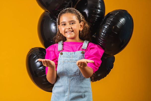 smiling little girl with black balloons on black friday. low price festival - Foto, Imagen