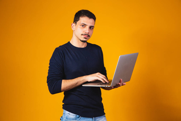 Portrait of boy holding laptop working in hands isolated over yellow background. - Fotografie, Obrázek
