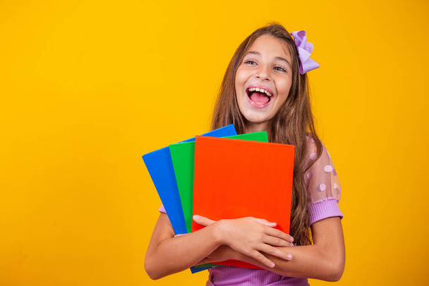 Beautiful smiling girl holding books going to school. close up portrait, isolated yellow background, childhood. child hugging notebooks. lifestyle, interest, hobby, free time, free time - Foto, afbeelding