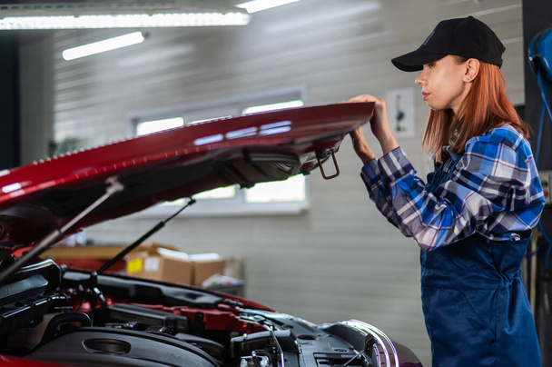 Woman auto mechanic opens the hood of a car in a car service - Foto, Bild
