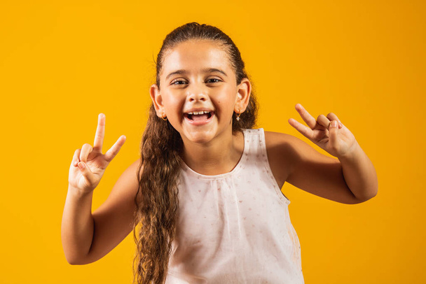 adorable little girl making v sign on yellow background. good vibe peace and love - Zdjęcie, obraz