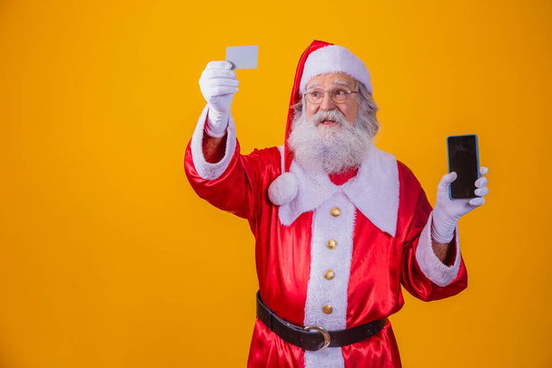 Portrait of a handsome Santa Claus holding credit card and smartphone with blank screen for text in his hand. - Foto, Bild