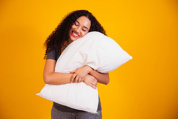 Photo of a dreamy afro girl hugging sleepy pillow on yellow background with free space for text. - Φωτογραφία, εικόνα