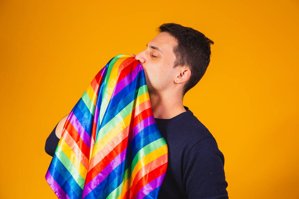 Gay pride. Homosexual boy kissing lgbt flag on yellow background. - Photo, image