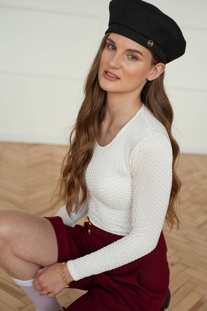 portrait of a young beautiful woman in a cap with long hair in a white shirt and a black skirt  - Foto, imagen