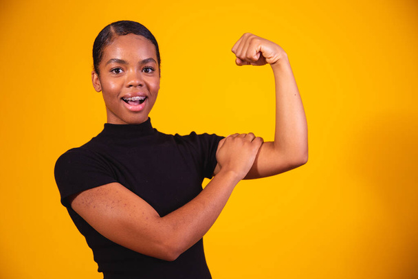 We can do it. Woman's fist of female power. Woman victim of racism. Abuse at work. The feminine power. Female empowerment. The strength of women. Yellow background. - Foto, Bild