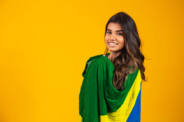 Brazilian supporter. Brazilian woman fan celebrating on soccer or football match on yellow background. Brazil colors. - 写真・画像