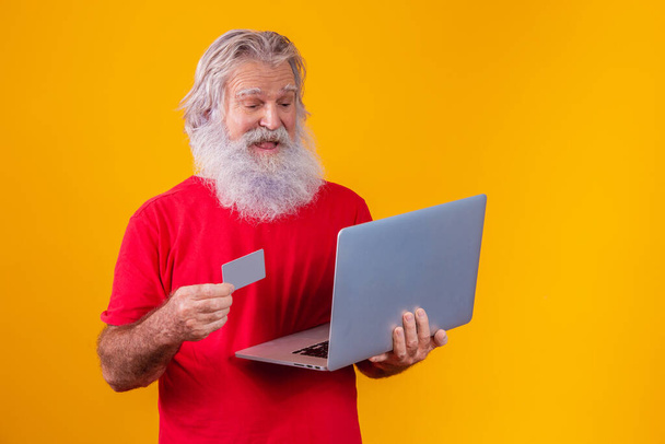 Elderly man holding laptop computer and bank credit card. Online shopping transaction. Mobile banking cashless method. - Zdjęcie, obraz