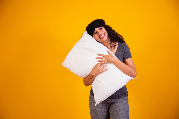 Photo of an afro girl hugging pillow on yellow background. Closeup of young girl holding a pillow in her hands. sleep concept - Foto, immagini