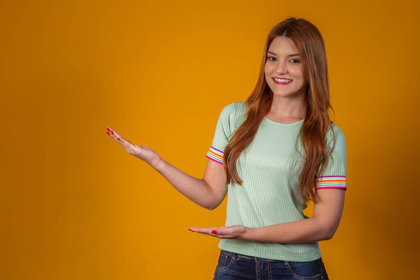 Red-haired young woman pointing on free space for text on yellow background. - Foto, Imagen