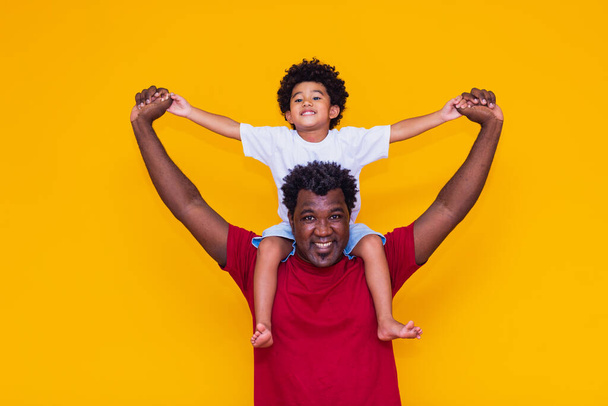Apa és afro fiú sárga háttérrel mosolyog és játszik. Apák napja koncepció - Fotó, kép