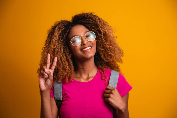 young afro with backpack on his back on yellow background. Young student smiling with glasses - Fotoğraf, Görsel