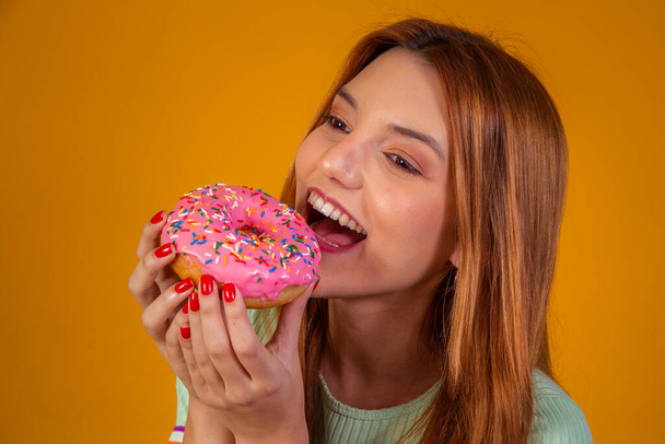 girl eating pink donuts on yellow background. - Photo, image