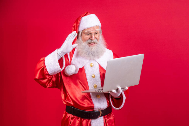 Santa Claus using a laptop on red background. - Foto, Imagen