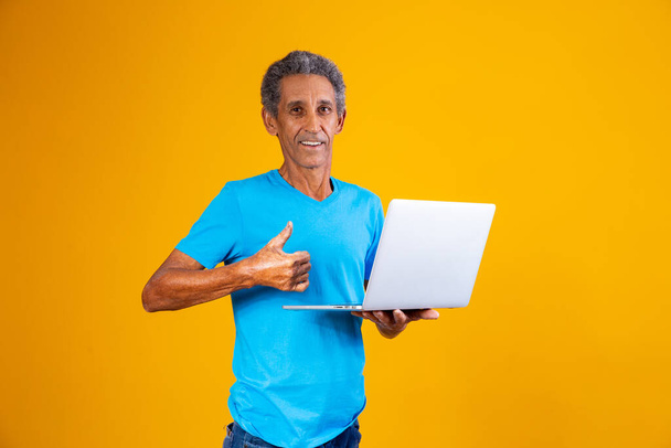 ηλικιωμένος άνδρας με ψώνια laptop ή εργάζεται online. Μεγαλύτερος με τον αντίχειρά του ψηλά κρατώντας ένα φορητό υπολογιστή. - Φωτογραφία, εικόνα