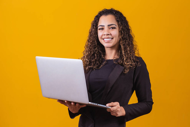Portrait of young woman in executive outfit with laptop on yellow background. Businesswoman working with laptop - Photo, image