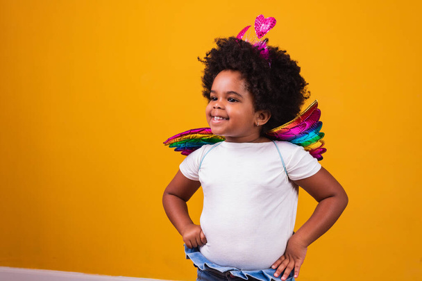 rozkošné afro dívka oblečená v barevné oblečení na žlutém pozadí. Dětský den. afro dívka s kostýmem - Fotografie, Obrázek