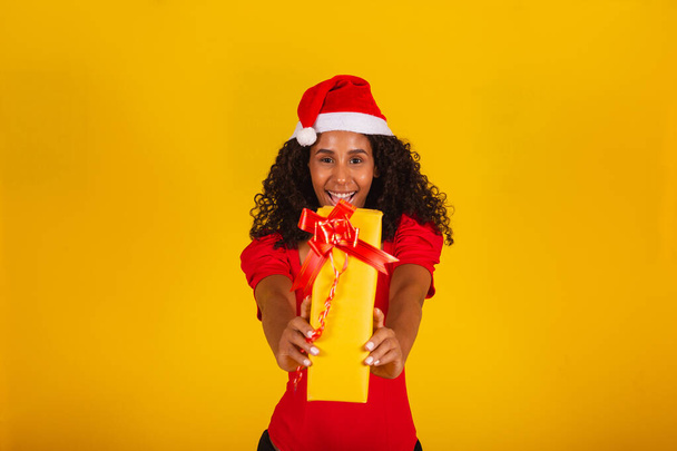Beautiful black woman in santa claus hat holding merry christmas gift on yellow background. - Valokuva, kuva