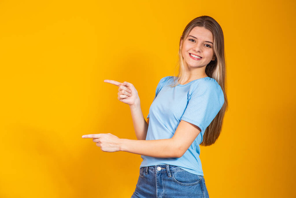 Caucasian smiling young woman pointing with two fingers to the side with free space for text. - Foto, imagen