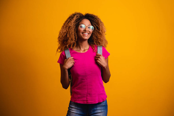 young afro with backpack on his back on yellow background. Young student smiling with glasses - Фото, изображение