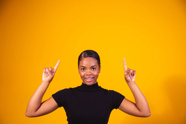 closeup of afro woman smiling on yellow background pointing up in space for text. - Fotografie, Obrázek