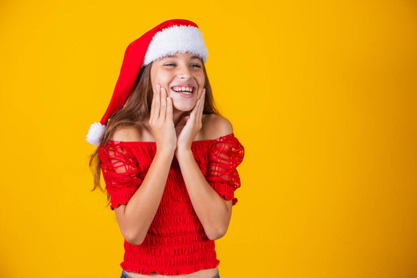 Portrait of a  caucasian smiling girl in a Santa hat on a yellow background. Christmas and happines concept. Close up, copy space - Foto, immagini