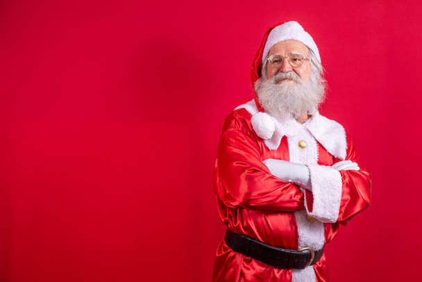 Santa Claus crossed arms on red background. Kind bearded Santa Claus with arms folded over red background. Studio shot of realistic Santa Claus. - Foto, immagini