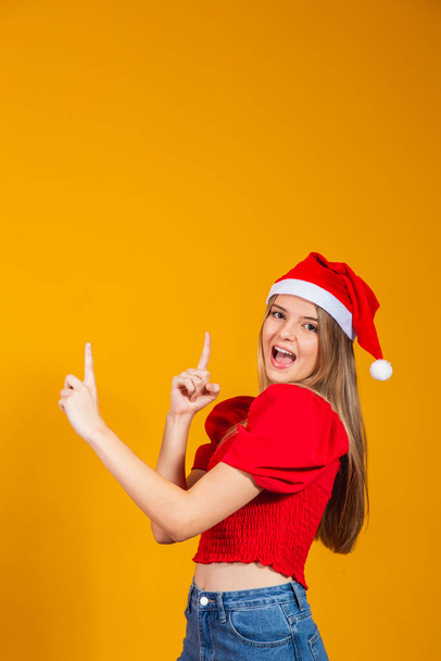 Close up photo positive girl in santa claus hat pointing forefinger, copyspace direct way x-mas christmas newyear ads promotion isolated yellow color background - Fotografie, Obrázek
