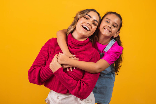 Photo of a beautiful young mommy holding her arms hugging her little daughter good mood adorable sincere heart feelings in the back jeans t-shirts isolated with yellow color background - Fotografie, Obrázek