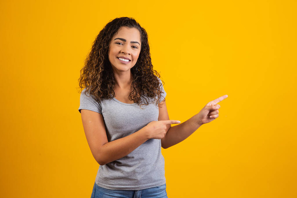 Afro woman pointing in yellow background with space for the text - Foto, immagini