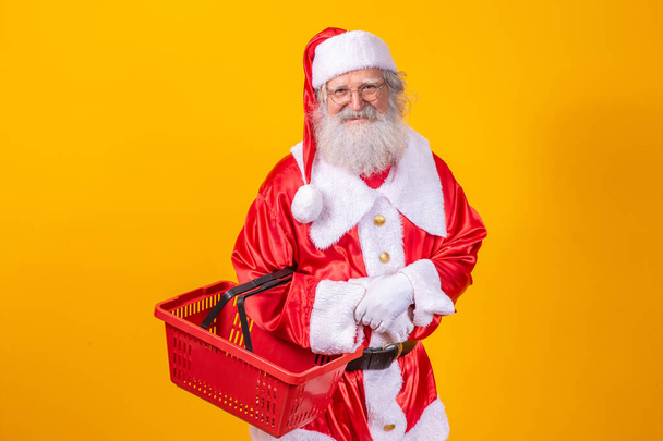 Santa Claus holding an empty shopping basket looking at the camera smiling. - Photo, Image