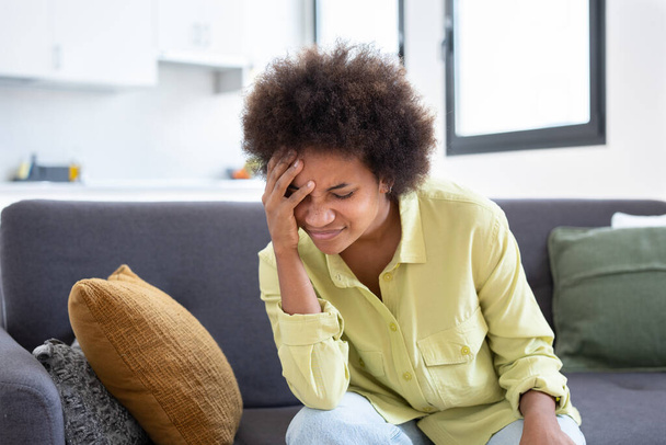 Upset stressed young african woman massage temples feel strong headache concept, frustrated tired black girl touching aching head suffer from migraine high blood pressure sitting on sofa at home - Photo, Image