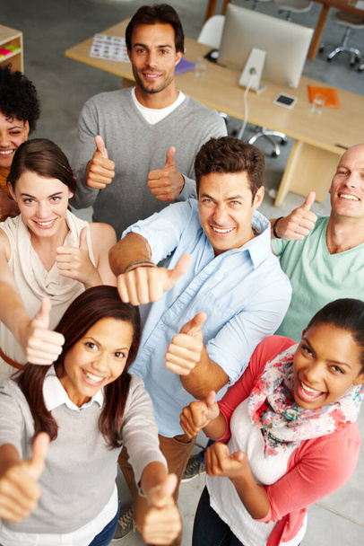 Passionate and positive about their service. High angle view portrait of a group of multi-ethnic people holding thumbs up in a work environment - Photo, Image
