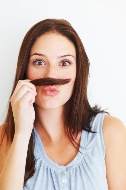 Comic, portrait and a woman with hair moustache isolated on a white background in studio. Smile, funny and a young girl being crazy, making face and playing with hairstyle for comedy on a backdrop. - Foto, Imagen