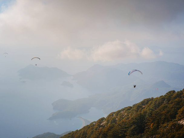 Gökyüzünde paraşütle atlıyor. Bulutlu bir günde denizin ve dağların üzerinde uçan paraglider ikilisi. Türkiye 'nin Oludeniz kentindeki Paraşütçü ve Mavi Göl manzarası. Olağanüstü bir spor. Peyzaj - Fotoğraf, Görsel
