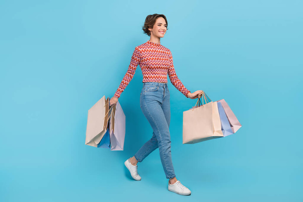 Full length photo of adorable sweet lady wear pink shirt walking holding shopping packages isolated blue color background. - Fotó, kép