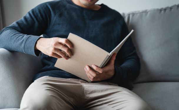 Man reading the notebook sitting on the sofa at home. - Φωτογραφία, εικόνα