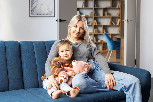 Young pregnant woman and her son sit on sofa at home, little boy spend time together, enjoy communication feeling kicks of unborn baby - Photo, image