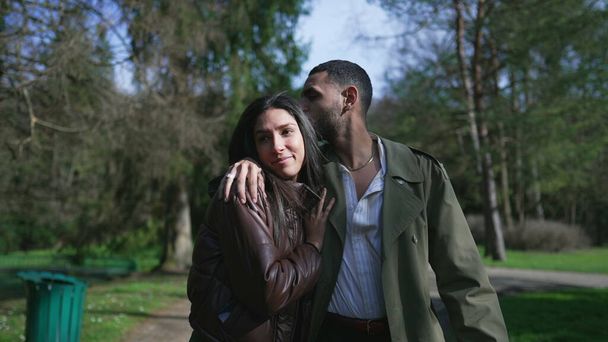 A Middle Eastern couple wrapped in love, strolling outdoors in a park with beaming smiles and affectionate embrace during a beautiful sunny day - Photo, Image