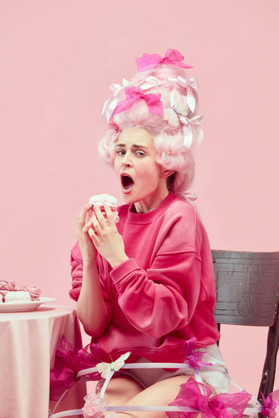 甘い姫。ピンク色のスタジオの背景にエキサイティングな顔を持つマシュマロを食べる大きなピンクのウィッグを身に着けている肖像空腹の女王。時代、現代とルネサンス、美しさ、歴史的概念の比較 - 写真・画像