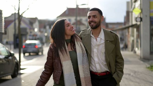 Una feliz pareja del Medio Oriente caminando juntos por la calle de la ciudad. Tracking shot de un hombre árabe con las manos alrededor alegre chica - Foto, Imagen