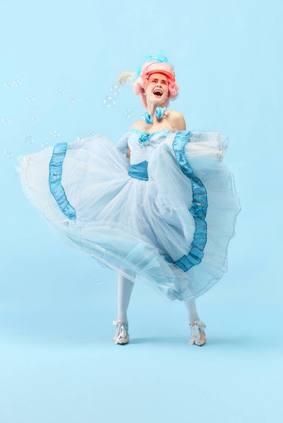 Stilvoll und schön. Porträt mit Prinzessin, Königin im Kreis mit ihrem Kleid und lächelnd über blauem Studiohintergrund. Konzept des Epochenvergleichs, Moderne, Barock, Schönheit, Mode, Emotion - Foto, Bild
