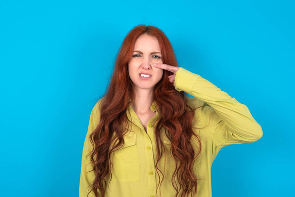 Jeune femme rousse caucasienne portant une chemise verte sur fond bleu pointant malheureux de boutons sur le front, infection laide de la tête noire. Acné et problème de peau - Photo, image