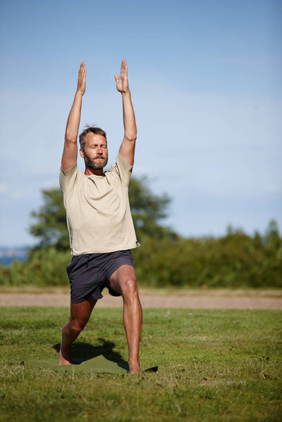 Focused while going through his posture sequence. Full length shot of a handsome mature man doing yoga outdoors - Photo, Image