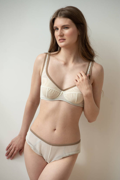 mooie jonge vrouw in een witte lingerie op een lichte achtergrond - Foto, afbeelding