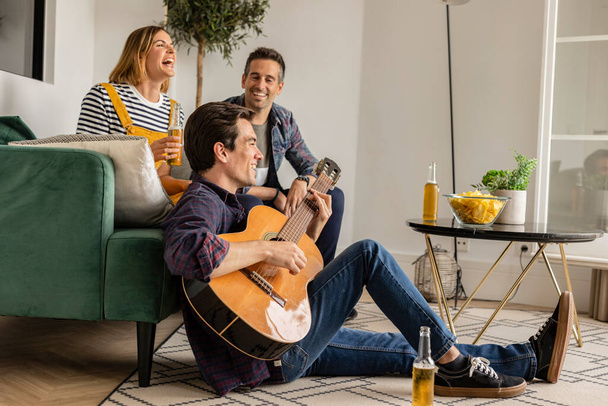 φίλοι στο σπίτι διασκεδάζουν παίζοντας κιθάρα πίνοντας μπύρα - Φωτογραφία, εικόνα