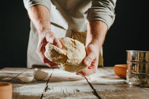 Close-up of male hands holding raw dough against black background. Selective focus. - Foto, Imagem
