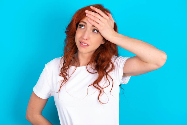 redhead woman wearing white T-shirt over blue background touching forehead, hears something surprising, glad receive good news, feels relieved. Almost got in trouble. - Photo, Image