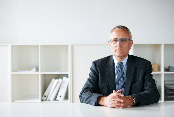 Stern face of the corporate world. a senior businessman sitting at a table - Foto, imagen